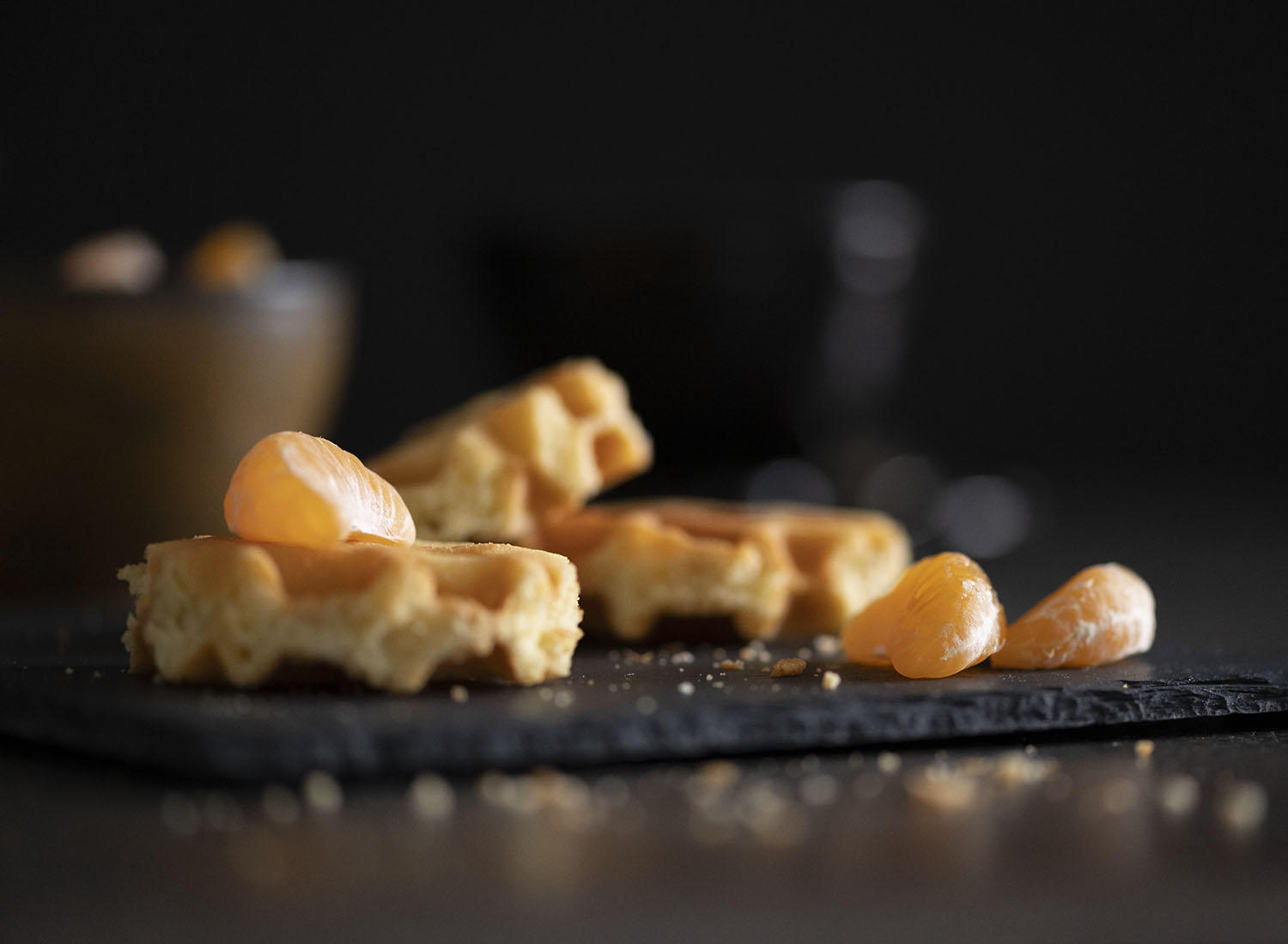 Unsere frisch gebackenen Belgischen Waffeln sind auf einer Kaffeetafel angerichtet. Wir haben eine Nahaufnahme von einer Waffel gemacht und auf sie eine frische Mandarine gelegt.