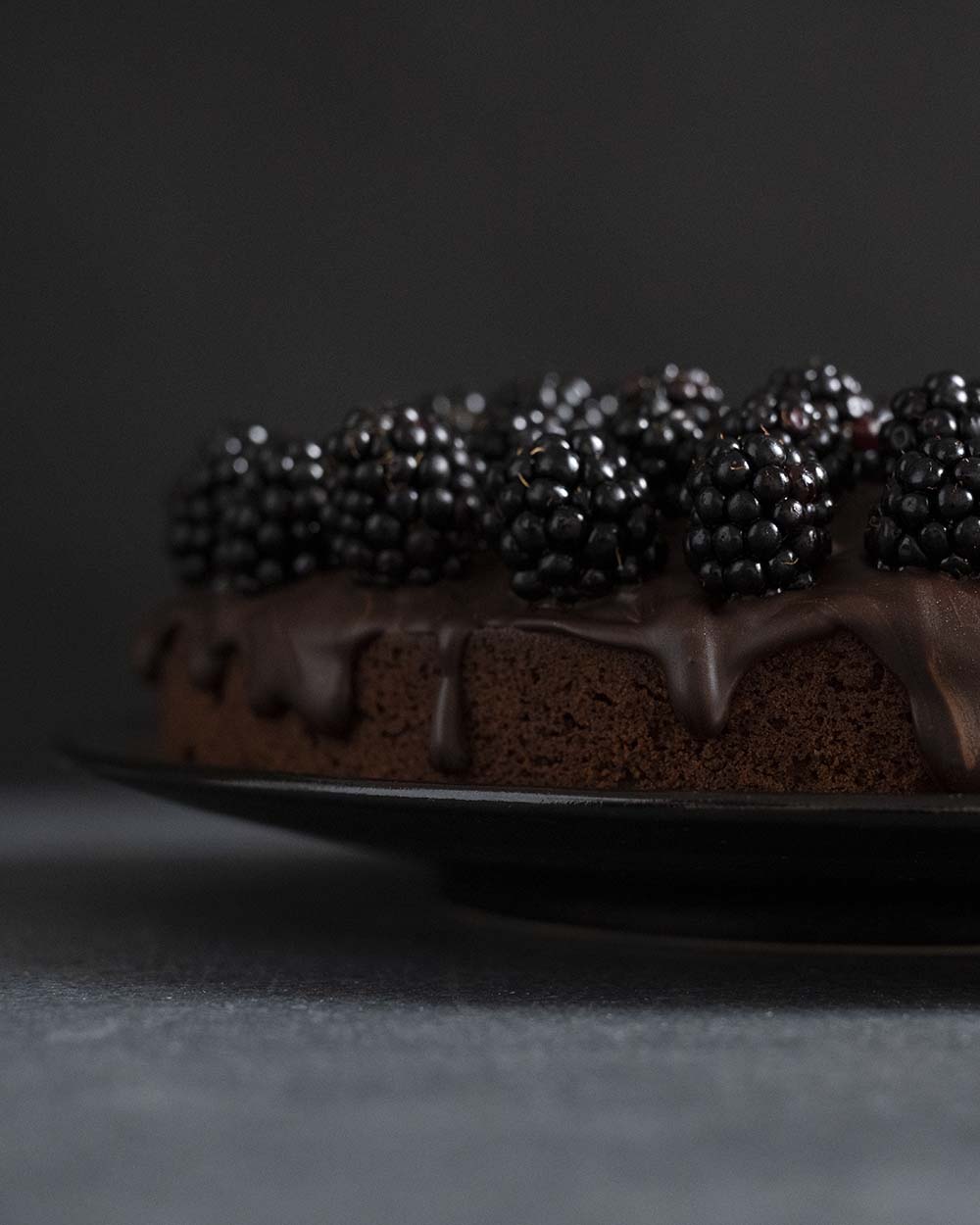 Ausschnitt unseres ferti dekorierten und lasierten Schokoladenkuchen mit Brombeeren. An der Seite läuft etwas geschmolzene Schokolade herunter.