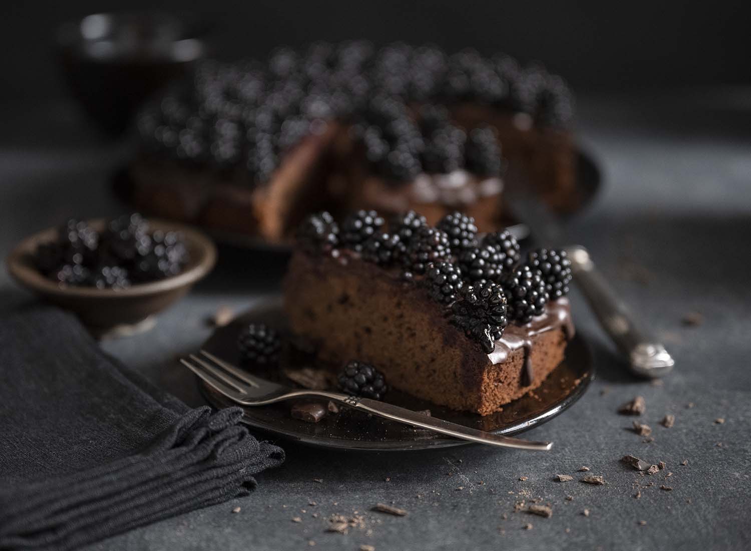 Ein Stück Schokoladenkuchen mit Brombeeren auf einem Teller.