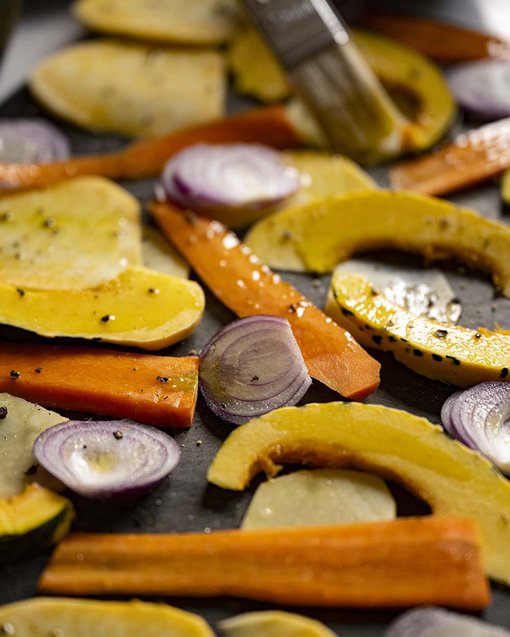 Nahaufnahme auf die verschiedenen Sorten Gemüse, darunter Kürbis, Möhre und Zwiebeln. Bevor wir unser Ofengemüse in den Ofen scheiben, streichen wir die einzelnen Gemüsesorten mit Öl ein und struen Salz und Pfeffer darauf.