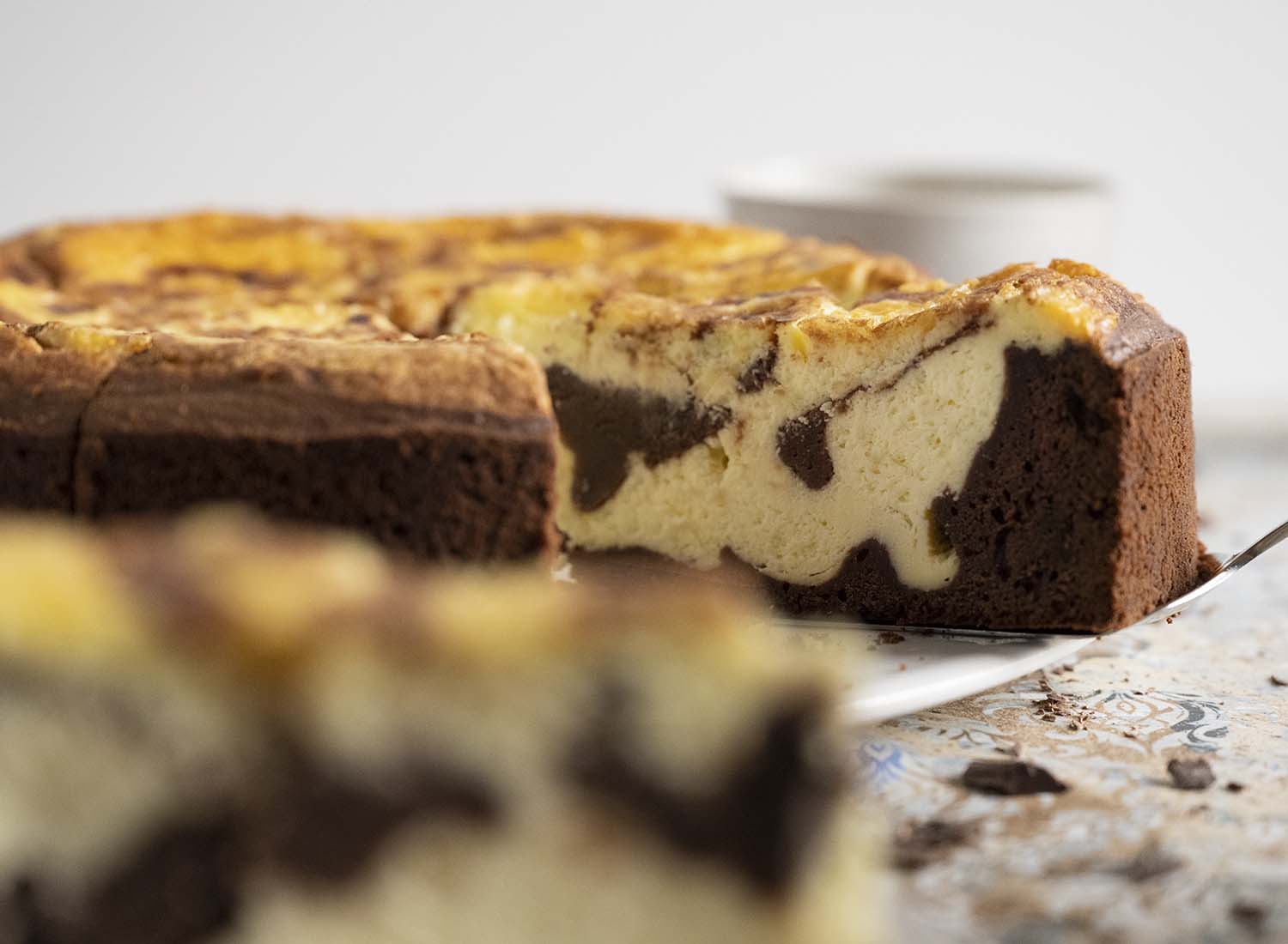 Ein Tortenheber steckt unter einem Stück Schokoladenkuchen mit Cheesecakefüllung. Gleich heben wir das Stück Kuchen auf einn Teller, Im Vordergrund ist ein zweites Stück Kuchen zu sehen, das bereits auf einem Teller steht. Dieses Bild ist aufgenommen im Querformat.